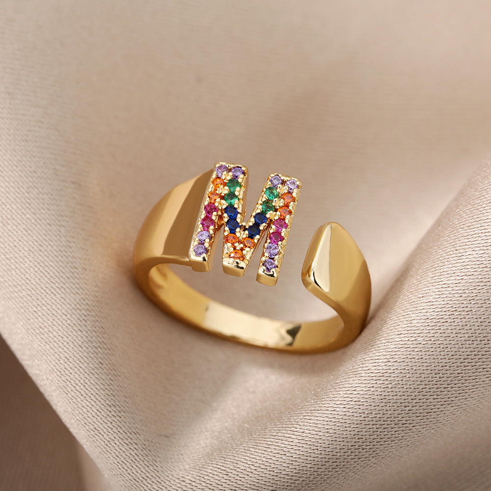 Anel com design vazado de 26 letras, cravejado com microzircônias coloridas e banhado a ouro 18K.