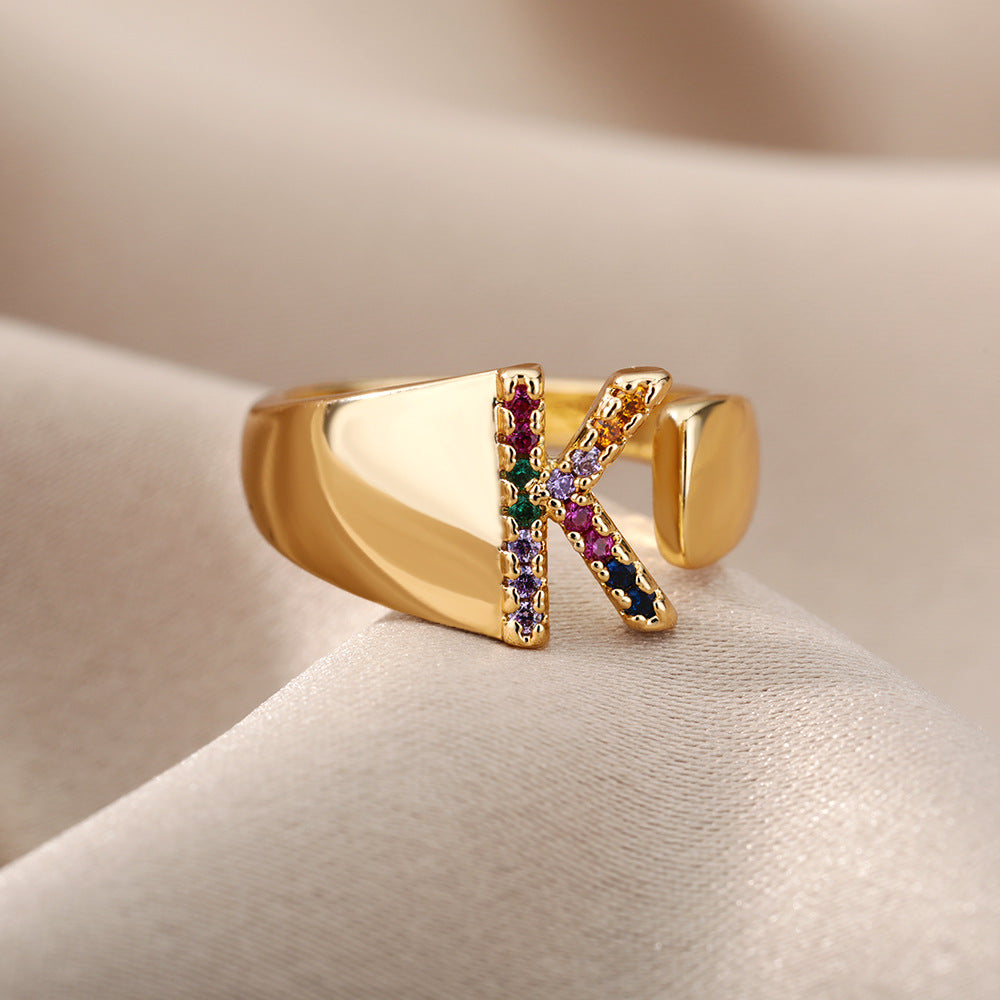 Anel com design vazado de 26 letras, cravejado com microzircônias coloridas e banhado a ouro 18K.