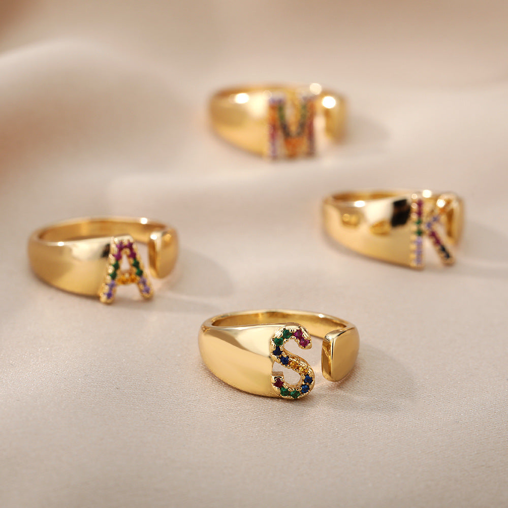 Anel com design vazado de 26 letras, cravejado com microzircônias coloridas e banhado a ouro 18K.